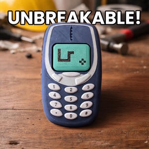 Op de afbeelding: Een blauwe retro-stijl mobiele telefoon met witte knoppen en een groen scherm met een gepixeld slangenspel. Het woord "UNBREAKABLE!" staat in het wit boven de telefoon. De telefoon ligt op een houten oppervlak.