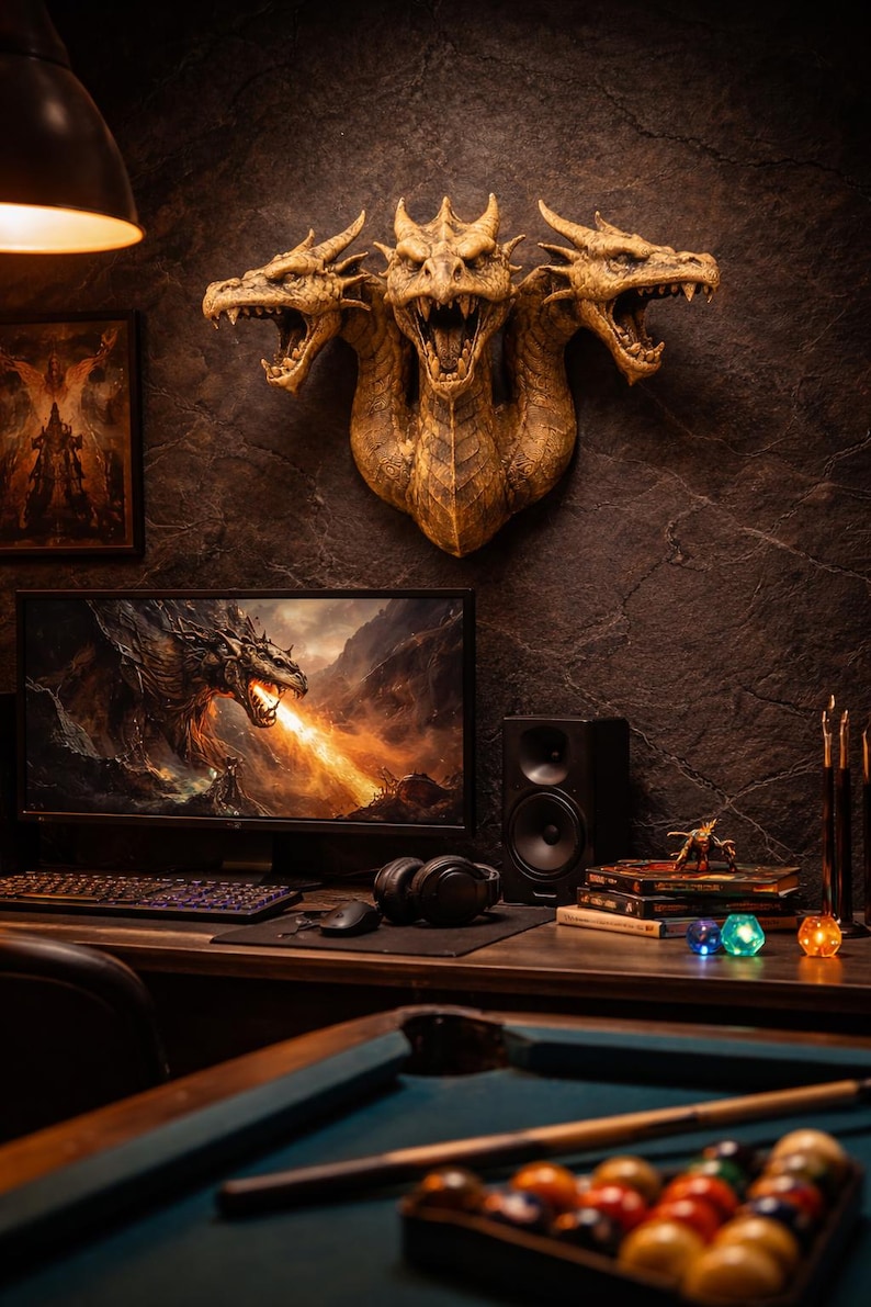 May include: A three-headed dragon wall sculpture in gold tones is mounted on a dark textured wall. A computer monitor displays a dragon breathing fire. A desk with a keyboard, mouse, and headphones is in front of the monitor. A pool table is in the foreground.