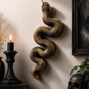 May include: A wall-mounted snake sculpture featuring a textured, coiled body with a gradient of dark black and metallic gold tones. The snake is depicted in an S-shaped curve with its head pointing upward and a small, thin tongue protruding.