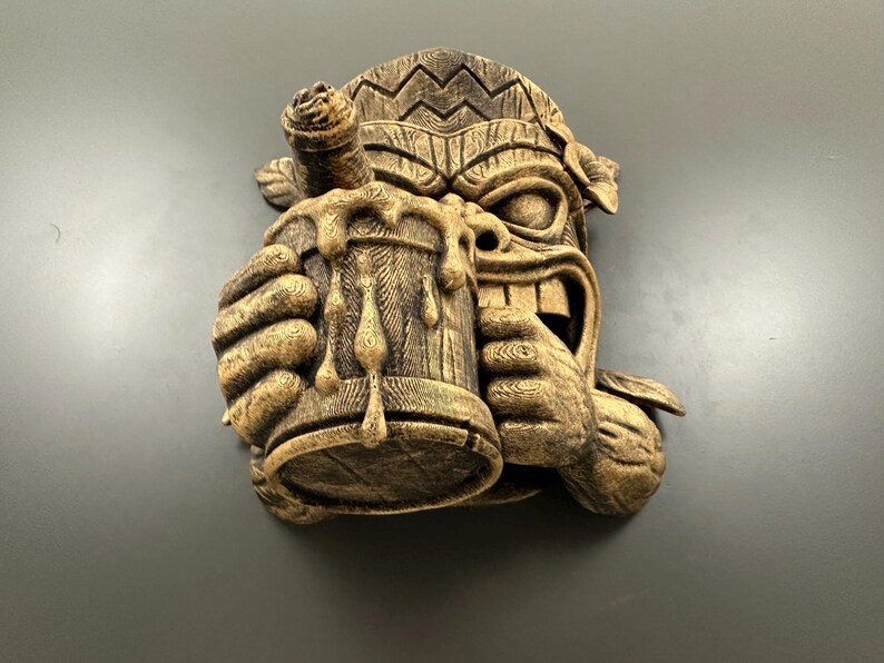 May include: A carved wooden tiki mask with a beer stein. The mask has a wide grin and is holding a wooden mug overflowing with dripping liquid. The tiki is brown with carved details and is a decorative wall hanging.