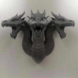 May include: A gray, three-headed dragon sculpture with open mouths and detailed scales. The sculpture is mounted on a wall and has a menacing expression. The dragon's heads are positioned to the left, center, and right.
