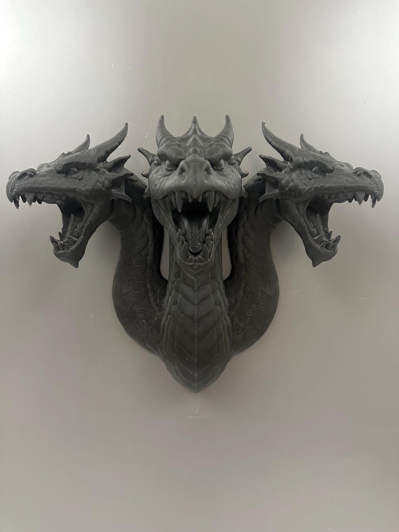 May include: A gray, three-headed dragon sculpture with open mouths and detailed scales. The sculpture is mounted on a wall and has a menacing expression. The dragon's heads are positioned to the left, center, and right.