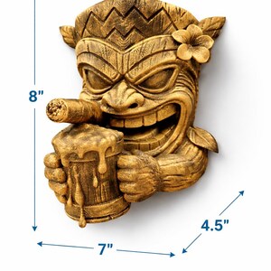 May include: A detailed, golden-brown Tiki mask wall hanging. The mask is 8 inches tall, 7 inches wide, and 4.5 inches deep. It features a smiling face, a cigar, and a mug of beer. A flower adorns the side of the head.