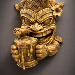 May include: A golden-colored Tiki mask sculpture with a smiling face, holding a beer mug and a cigar. The mask has a flower on its head and is carved with intricate details, perfect for tropical decor.