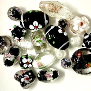 May include: Assortment of black and white glass beads with floral and geometric designs. The beads are various shapes and sizes, including round, oval, and rectangular.