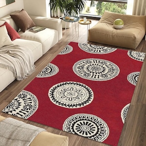 Puede incluir: Una alfombra rectangular roja con un patrón repetido de grandes diseños florales circulares en blanco y negro. La alfombra está colocada sobre un suelo de madera en un salón.