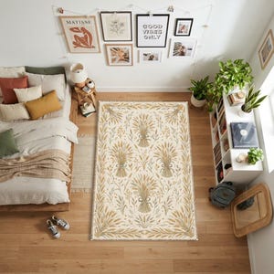 Könnte beinhalten: Ein rechteckiger Teppich mit einem sich wiederholenden Muster aus Weizengarben in Gold-, Beige- und gedämpften Grüntönen auf cremefarbenem Grund. Das Design zeigt stilisierte Halme und Blätter in einer symmetrischen, botanischen Anordnung.