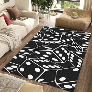 May include: A black and white area rug featuring a repeating pattern of dice. The dice are rendered in a 3D style, with white dots on a black background. The rug is rectangular and placed on a hardwood floor.