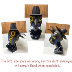 May include: A black and blue mask with a beak and a hat, displayed on a black bust. The mask has yellow eye accents and a red beak. The text at the bottom says, "The left-side eyes will move, and the right-side eyes will remain fixed when completed."
