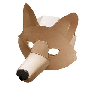 Puede incluir: Una máscara de zorro de cartón color canela con orejas puntiagudas, dos aberturas ovaladas para los ojos y un hocico prominente con una punta de nariz negra. La máscara está hecha de paneles de papel plegados con una forma geométrica.