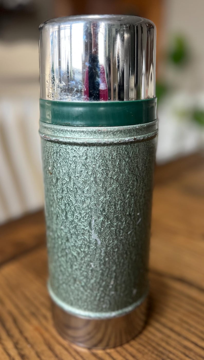 Puede incluir: Termo verde y plateado vintage. El termo tiene un cuerpo verde texturizado, una tapa plateada y una banda verde. La parte inferior tambi&eacute;n es plateada. Dise&ntilde;ado para mantener l&iacute;quidos calientes o fr&iacute;os.