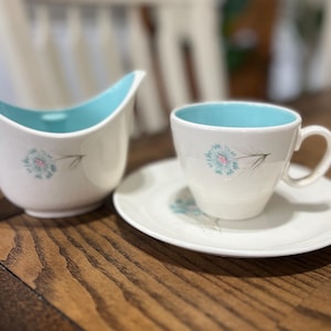 Peut inclure: Une tasse en céramique blanche avec une anse noire et l'inscription "But First, Coffee" en noir, dans une police manuscrite. La tasse est posée sur une surface blanche.