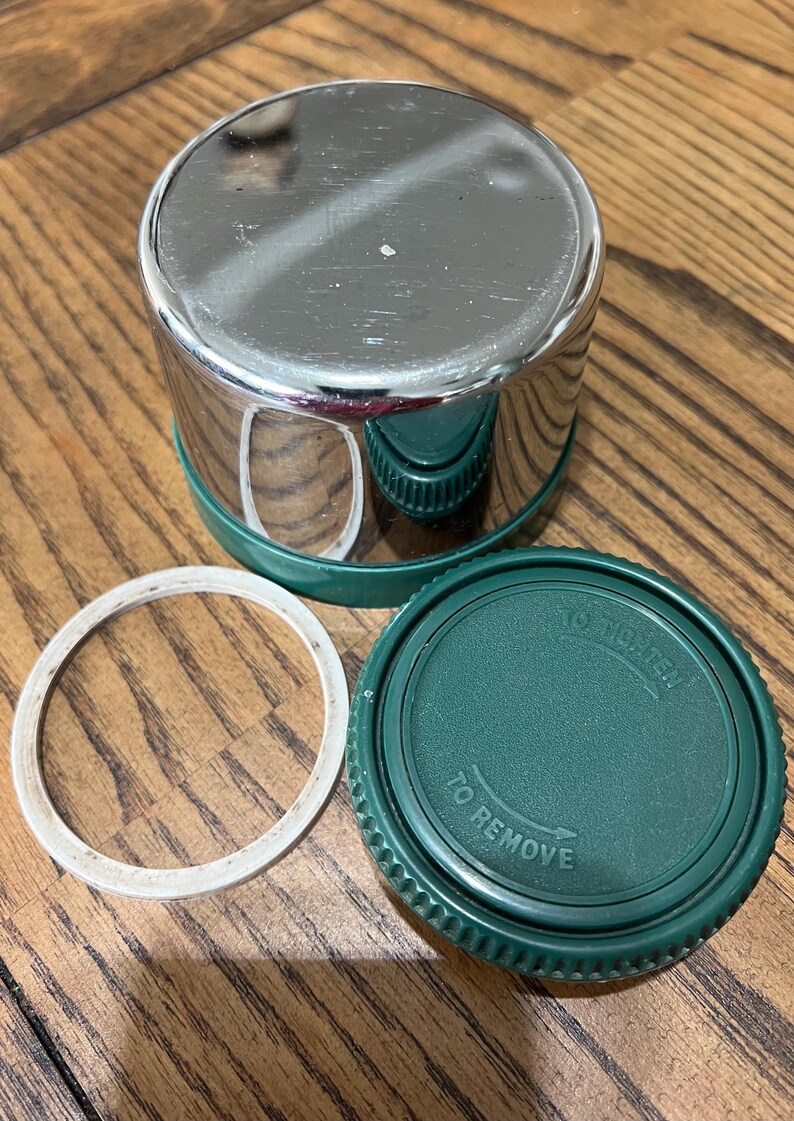 Puede incluir: Un recipiente de acero inoxidable brillante con base y tapa verdes, junto con un anillo de goma blanco. La tapa tiene las palabras "TO REMOVE" y "TO TIGHTEN" impresas. El recipiente est&aacute; dise&ntilde;ado para el almacenamiento.