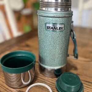 Puede incluir: Termo Aladdin Stanley vintage en verde con tapa y base de acero inoxidable. El termo tiene un acabado texturizado y el logotipo de Aladdin Stanley. Incluye una taza, tapa y sello.