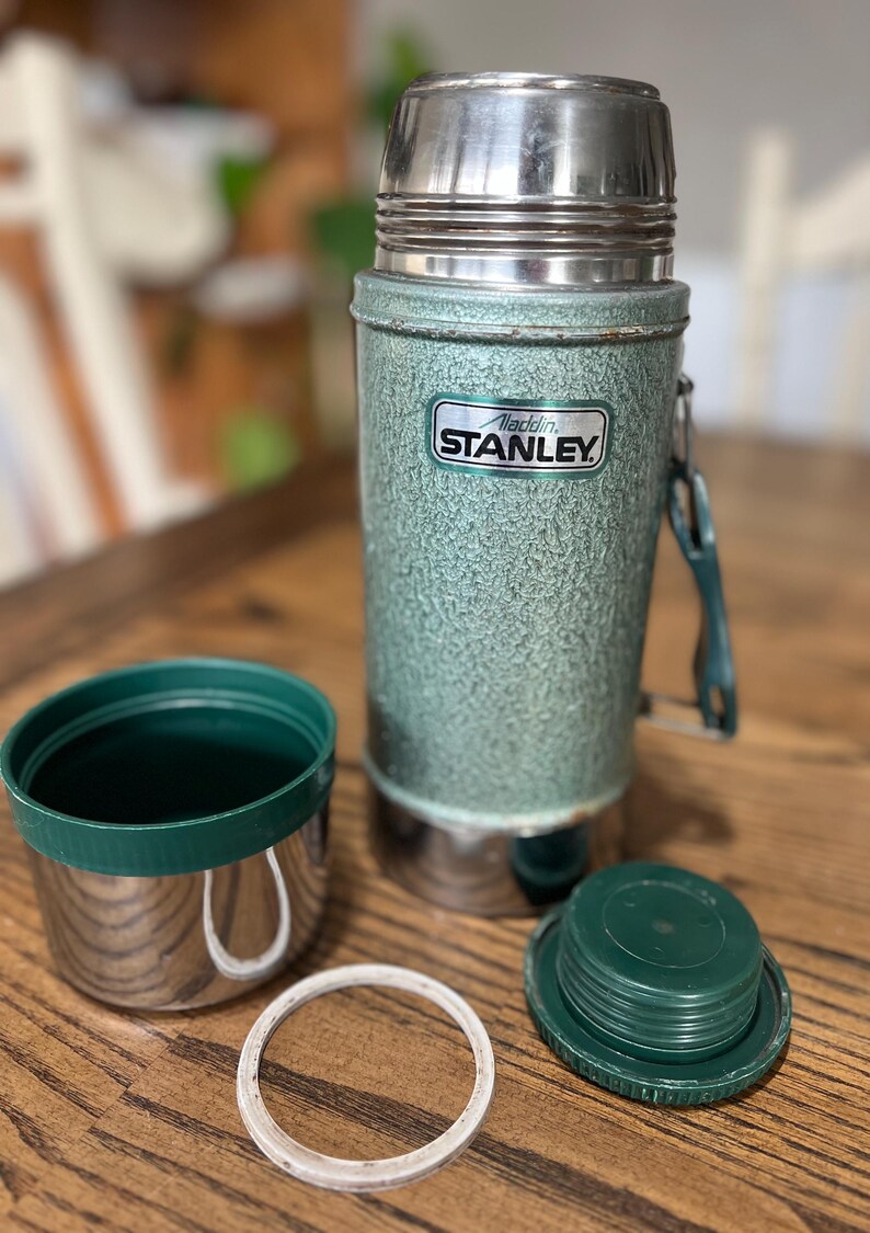 Puede incluir: Termo Aladdin Stanley vintage en verde con tapa y base de acero inoxidable. El termo tiene un acabado texturizado y el logotipo de Aladdin Stanley. Incluye una taza, tapa y sello.
