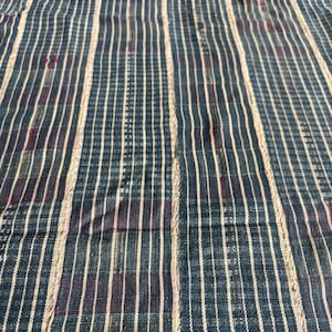May include: A woven textile fabric featuring a vertical striped pattern in shades of dark blue, charcoal, and off-white. The design consists of alternating thin and thick stripes with a subtle grid-like texture throughout the material surface.