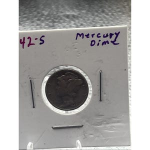 Puede incluir: Una moneda Mercury Dime, presentada en un soporte protector. La moneda es de color metálico oscuro, y el soporte tiene texto escrito a mano que dice "42-5" y "Mercury Dime". La moneda está fechada en 1942.