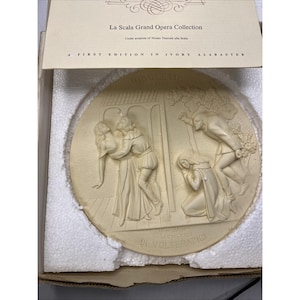 以下が含まれることがあります： ラ・スカラ・グランド・オペラ・コレクションの象牙アラバスターレリーフ。リゴレットのシーンを描いています。丸いプラークには、クラシックな衣装の人物が描かれており、「RIGOLETTO」や「DI VOLTERADICI」などのテキストがあります。商品は箱に入っています。