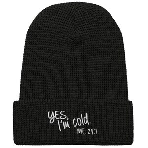 以下が含まれることがあります： 白の文字で「Yes, I'm cold. ME 24:7」と書かれた黒いニット帽。折り返しのあるつばと、ワッフルのような質感のパターンが特徴です。冬のアクセサリー。
