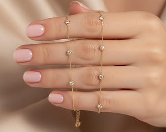 May include: A delicate gold bracelet featuring multiple round, clear gemstones. The bracelet is displayed against a soft, neutral background, highlighting the jewelry's elegant design. The gemstones are evenly spaced along the fine gold chain.