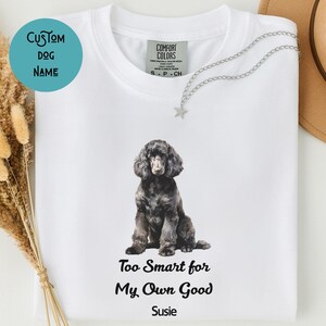 Op de afbeelding: Wit T-shirt met een illustratie van een zwarte poedel. Het shirt toont de tekst "Too Smart for My Own Good" en de naam "Susie". Een aangepaste hondennaamcirkel staat linksboven.