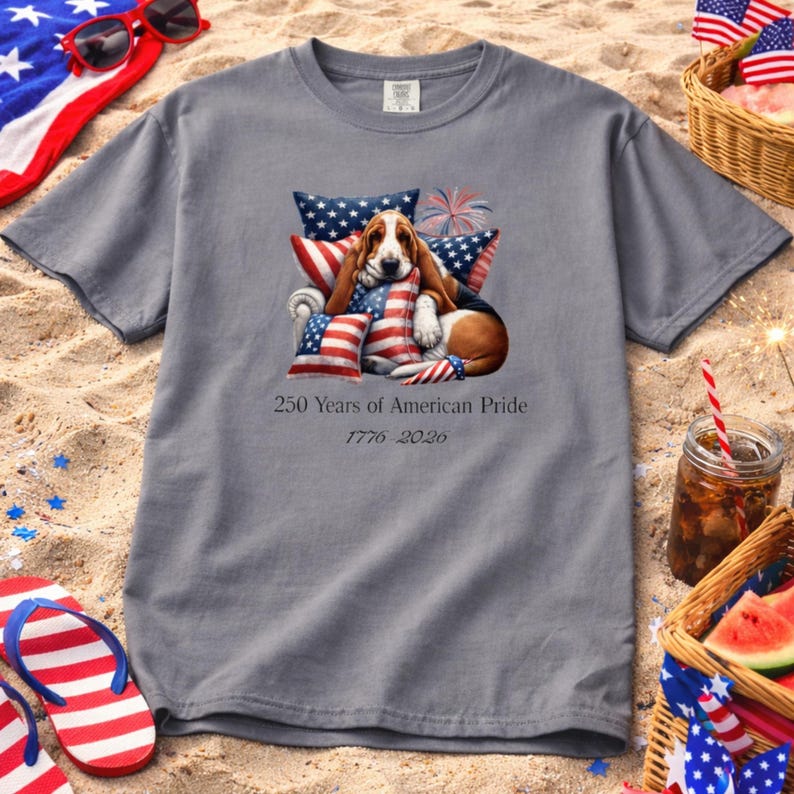 Patriotic dog lover shirt grey tee styled on beach sand with flip flops, picnic basket, watermelon, and 4th of July setup.