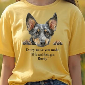 May include: Yellow t-shirt featuring a dog graphic with the text "Every move you make I'll be watching you Rocky". The dog has black, gray, and brown fur. The shirt is made of a soft material.