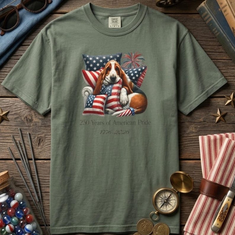 Basset hound 1776 2026 shirt in moss green with vintage Americana flat lay compass marbles and rustic wood background.