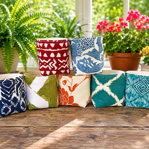 May include: A collection of seven small fabric storage baskets featuring various patterns and colors, including red, blue, green, orange, and teal. The baskets are arranged in a group on a wooden surface, showcasing diverse geometric and floral prints.