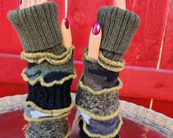 May include: A pair of olive green fingerless gloves with layered camouflage and black sections, trimmed with gold-colored stitching. The gloves are displayed on mannequin hands with red nail polish.