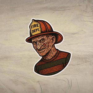 以下が含まれることがあります： 「FIRE DEPT.」の文字が入った消防士のヘルメットをかぶったキャラクターの、様式化されたイラストが描かれたステッカー。キャラクターは不気味な表情をしており、ストライプのセーターを着ています。ステッカーには白い縁取りがあります。