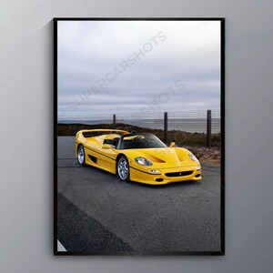 May include: A framed print featuring a bright yellow convertible sports car on a paved road. The car is the focal point, set against a backdrop of a cloudy sky and a distant fence. The text "SUPERCARSHOTS" is visible.