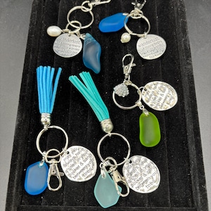 Peut inclure: Porte-clés avec divers breloques, dont du verre de mer, des pompons et des étiquettes métalliques gravées. Les porte-clés sont dotés d'une quincaillerie argentée et comportent des phrases telles que "wanderlust" et "may you always have a shell in your pocket & sand between your toes."