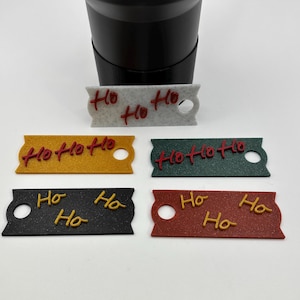 May include: A collection of colorful rectangular tags with the text "Ho Ho Ho" in a festive font. The tags are in various colors, including gray, yellow, green, black, and red. Each tag has a hole on one end.