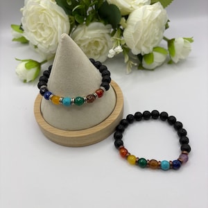 May include: Two beaded bracelets featuring black porous lava stone beads and a series of colorful, smooth, round gemstone beads in shades of red, orange, yellow, green, turquoise, blue, and purple, accented with small metallic spacer rings.