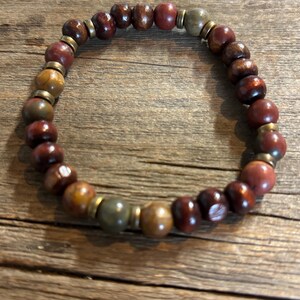 Puede incluir: Una pulsera el&aacute;stica compuesta por cuentas redondas en tonos marr&oacute;n oscuro, marr&oacute;n rojizo y verde oliva apagado. Las cuentas est&aacute;n intercaladas con peque&ntilde;os espaciadores met&aacute;licos planos de color lat&oacute;n que crean un patr&oacute;n circular repetitivo.