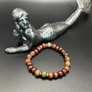 Puede incluir: Una pulsera el&aacute;stica compuesta por cuentas de piedra redondas y multicolores en tonos marr&oacute;n rojizo, bronceado y verde oliva, acentuadas con peque&ntilde;as cuentas espaciadoras met&aacute;licas de color oro antiguo en c&iacute;rculo.
