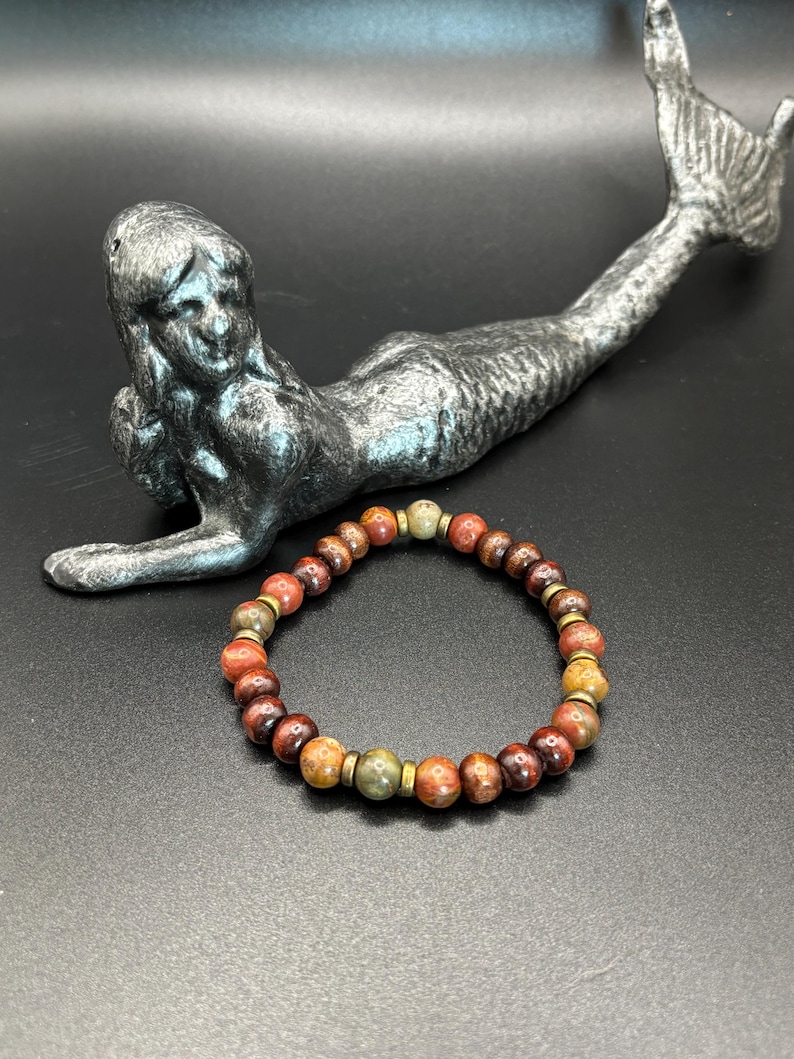 Puede incluir: Una pulsera el&aacute;stica compuesta por cuentas de piedra redondas y multicolores en tonos marr&oacute;n rojizo, bronceado y verde oliva, acentuadas con peque&ntilde;as cuentas espaciadoras met&aacute;licas de color oro antiguo en c&iacute;rculo.