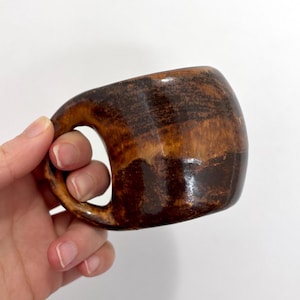 Peut inclure: Une tasse en céramique faite à la main avec une poignée arrondie unique. La tasse présente une riche palette de couleurs terreuses de bruns et de beiges, avec une finition brillante. Le design est organique et rustique, parfait pour le café ou le thé.