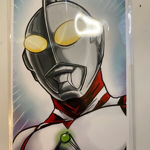 May include: A black and white illustration of a superhero with a red and white suit. The superhero has a silver helmet with a green gem on the chest. The background is a blue and white gradient.