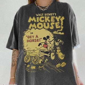 May include: Dark gray t-shirt featuring a vintage Mickey Mouse graphic. The design includes Mickey Mouse in a cart with a horse, with text that reads "WALT DISNEY'S MICKEY MOUSE" and "GET A HORSE!". The shirt is from Pepper Comfort Colors.