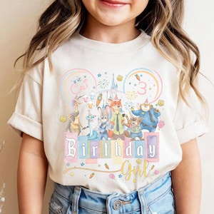 May include: A beige t-shirt with a colourful graphic of animated movie characters, a castle, and the words "Birthday Girl". The number "3" is also displayed. The shirt is worn by a child.