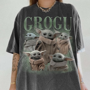 Puede incluir: Camiseta gris oscuro con la palabra "GROGU" en verde sobre un gr&aacute;fico de Grogu, tambi&eacute;n conocido como Baby Yoda, de The Mandalorian. El gr&aacute;fico muestra a Grogu en varias poses, vistiendo un abrigo marr&oacute;n.