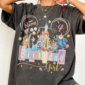 May include: Charcoal grey t-shirt with a vibrant graphic of cartoon characters, a castle, and the words "Birthday Girl". The design includes the number 4 and space for a name, ideal for a birthday party.