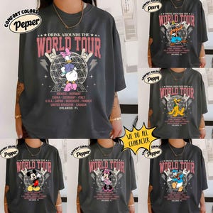 K&ouml;nnte beinhalten: Dunkelgraue T-Shirts mit verschiedenen Disney-Charakter-Designs. Jedes Shirt zeigt den Text "DRINK AROUND THE WORLD TOUR" in Pink, sowie eine Liste von L&auml;ndern und "ORLANDO, FL". Charaktere sind Daisy Duck, Goofy, Pluto, Mickey, Minnie und Donald Duck.