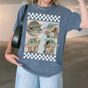 Pode incluir: Camiseta azul com um gr&aacute;fico de quatro pain&eacute;is de Grogu de The Mandalorian. Os pain&eacute;is mostram Grogu em diferentes poses, rodeado por um padr&atilde;o xadrez preto e branco. A camiseta &eacute; de estilo casual.