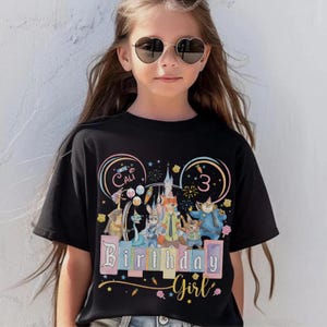 May include: Black t-shirt with a colourful graphic featuring cartoon characters, a castle, and the text "Birthday Girl" and "3". The shirt also has the name "Cali" in a circle.