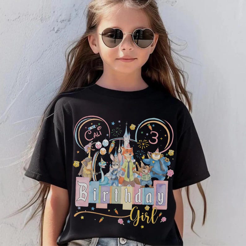 May include: Black t-shirt with a colourful graphic featuring cartoon characters, a castle, and the text "Birthday Girl" and "3". The shirt also has the name "Cali" in a circle.