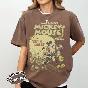 May include: Espresso-colored t-shirt featuring a vintage Walt Disney's Mickey Mouse graphic. The design includes Mickey Mouse in a horse-drawn carriage with the text "Get a Horse!". The shirt has a crew neck and short sleeves.