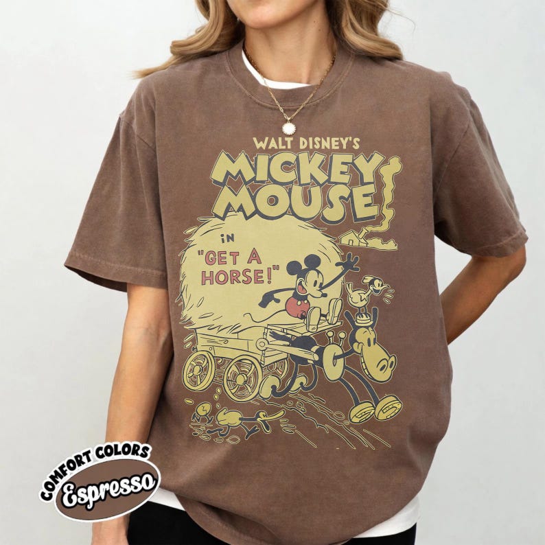May include: Espresso-colored t-shirt featuring a vintage Walt Disney's Mickey Mouse graphic. The design includes Mickey Mouse in a horse-drawn carriage with the text "Get a Horse!". The shirt has a crew neck and short sleeves.